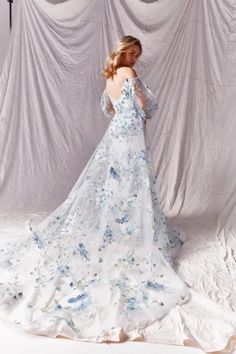 a woman is standing in front of a white backdrop wearing a dress with blue flowers on it