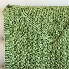 a green knitted blanket sitting on top of a white couch