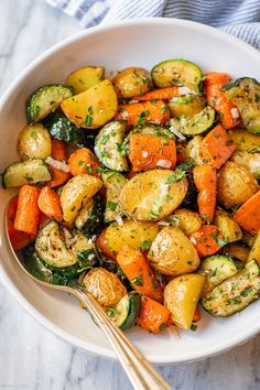 a white bowl filled with roasted vegetables on top of a marble counter next to a fork