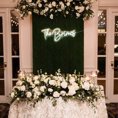 a table topped with white flowers and greenery under a neon sign that reads the bridals