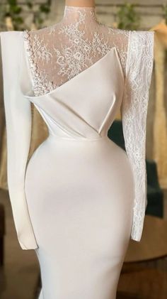 the back of a white dress with long sleeves and lace on it, in front of a mannequin