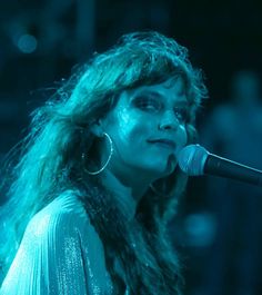 a woman with long hair standing in front of a microphone and singing into the microphone