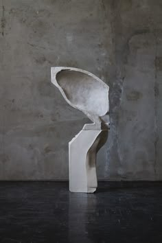 a white sculpture sitting on top of a black floor next to a cement wall with a plant growing out of it