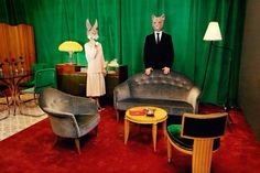 two people dressed up as rabbits standing in a living room with chairs and lamps on the floor