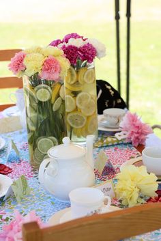 flowers and lemons are in vases on a table with plates, cups and teapots