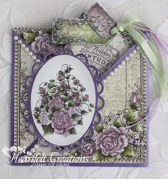 an ornate card with purple flowers and green leaves on the front, sitting on a white lace tablecloth