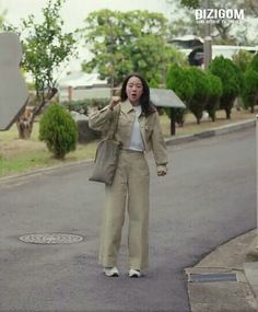 a woman standing on the side of a road holding her hand up to her ear