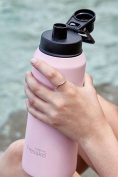 a woman holding a pink water bottle in her right hand while sitting on the beach