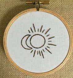 an embroidered sun and moon on a piece of fabric with a wooden hoop hanging from the wall