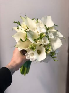 a bouquet of white flowers being held by a person's hand in front of a wall