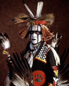 a man dressed in native american clothing with feathers on his head and hands, holding two birds