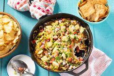 a pan filled with mexican food next to bowls of chips and tortilla chips