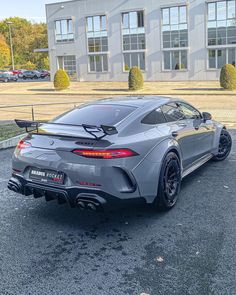 the rear end of a grey sports car parked in front of a large building with lots of windows