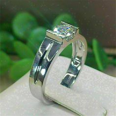 a white gold ring with a princess cut diamond on the side, sitting on top of a napkin