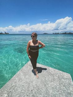 a woman standing on the edge of a pier in clear blue water, with her hands on her hips