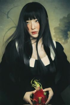 a woman with long black hair holding a red flower in her hands and looking at the camera