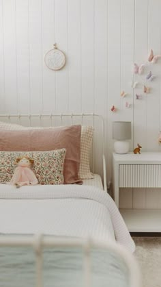 a white bed topped with pillows next to a night stand and table filled with stuffed animals