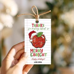 a hand holding a christmas card with an apple on it that says thanks for making school so merry and bright