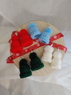 three crocheted baby booties are sitting on a wooden platter with red, white and green mittens