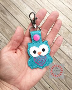 a hand holding a blue owl shaped keychain with a pink heart on it