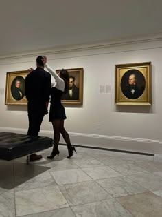 a man and woman are standing in front of some portraits on display at an art museum