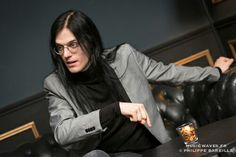 a woman with long hair and glasses sitting at a table in front of a black leather chair