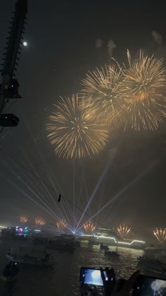 fireworks are lit up in the night sky over water and boats on the river below