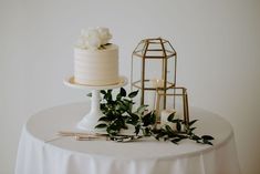 a table with a white cake and greenery on it, next to a candle holder