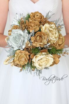 a bridal holding a bouquet of gold and silver flowers in her hands with pine cones on the side