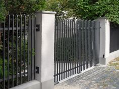 an iron fence is next to a white wall and trees in the background, along with cobblestone pavement