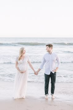 a pregnant couple holding hands on the beach