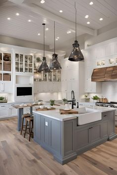 a large kitchen with white cabinets and gray island in the center is lit by two pendant lights