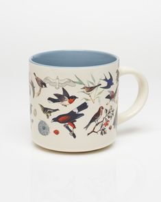 a coffee mug with birds painted on the side and blue rim, in front of a white background