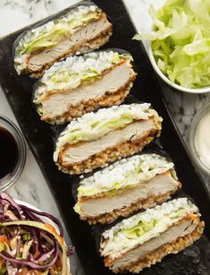 several slices of sushi on a black tray next to salad and dipping sauces