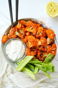 a bowl filled with cauliflower and celery sticks next to a lemon wedge