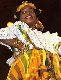 a woman in a colorful dress and headdress on stage with her hands behind her back