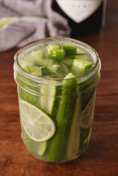 a mason jar filled with sliced cucumbers and limes on a wooden table