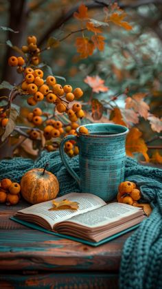 an open book and cup sitting on top of a wooden table next to leaves, pumpkins and berries