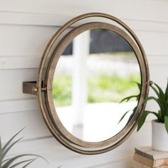 a round mirror hanging on the side of a white wall next to a potted plant