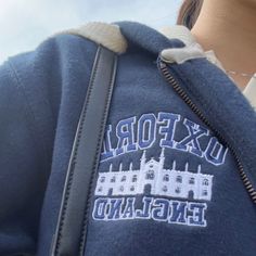 a person wearing a blue sweatshirt with the words oxford england on it and a castle in the background