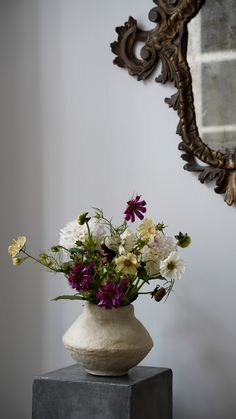 a vase filled with lots of flowers sitting on top of a wooden table next to a mirror