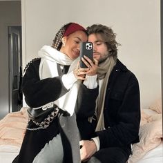 a man and woman sitting on a bed taking a selfie with their cell phone