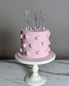 a pink cake with lots of hearts on it and forks sticking out of the top