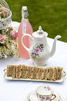 tea and sandwiches on a table with pink flowers in the backgroung area