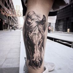 a man's leg with a horse tattoo on it and buildings in the background