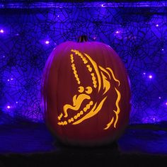 a carved pumpkin with an image of a dragon on it's face in front of purple lights