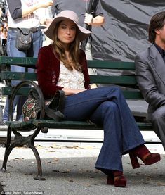 a woman sitting on top of a bench next to a man in a suit and hat