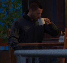 a man drinking from a coffee cup while standing in front of a table with chairs