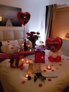 valentine's day decorations on a bed with candles and heart - shaped balloons in the background