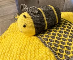 a crocheted stuffed animal laying on top of a yellow and black blanket next to a gray chair